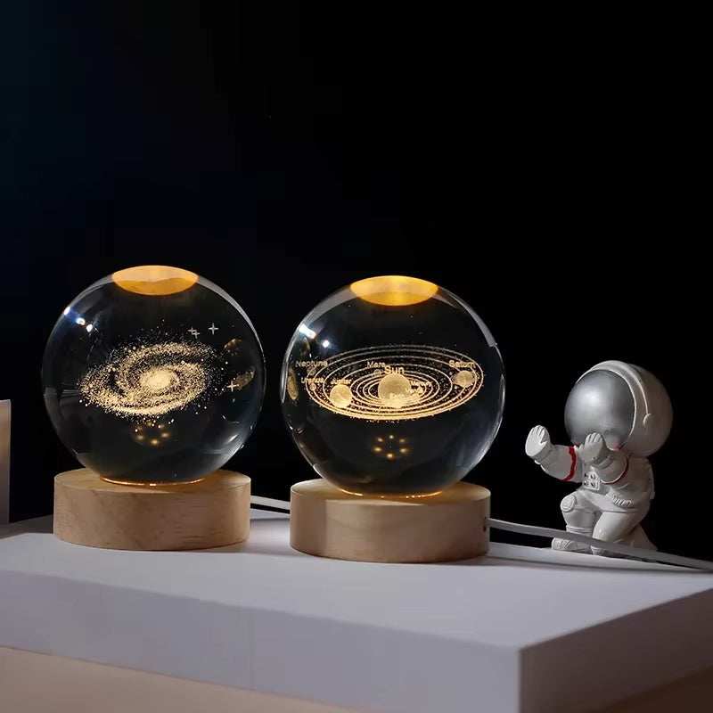 Two illuminated crystal balls with solar system design on wooden stands, accompanied by a small astronaut figurine.
