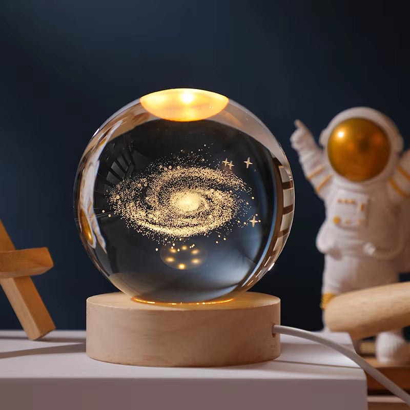 Glass ball with galaxy design on a wooden base, next to an astronaut figurine.