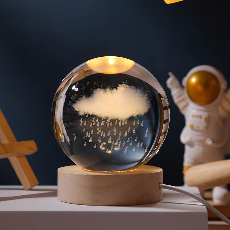 Glass orb with cloud and raindrop design on a wooden base, with an astronaut figure in the background.